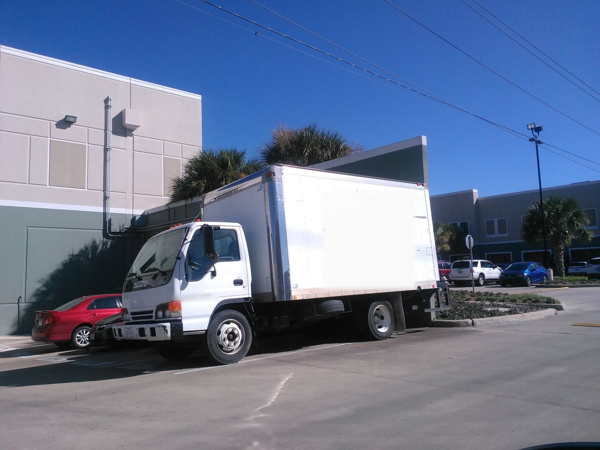 White cab-over box truck parked outside a building under palm trees